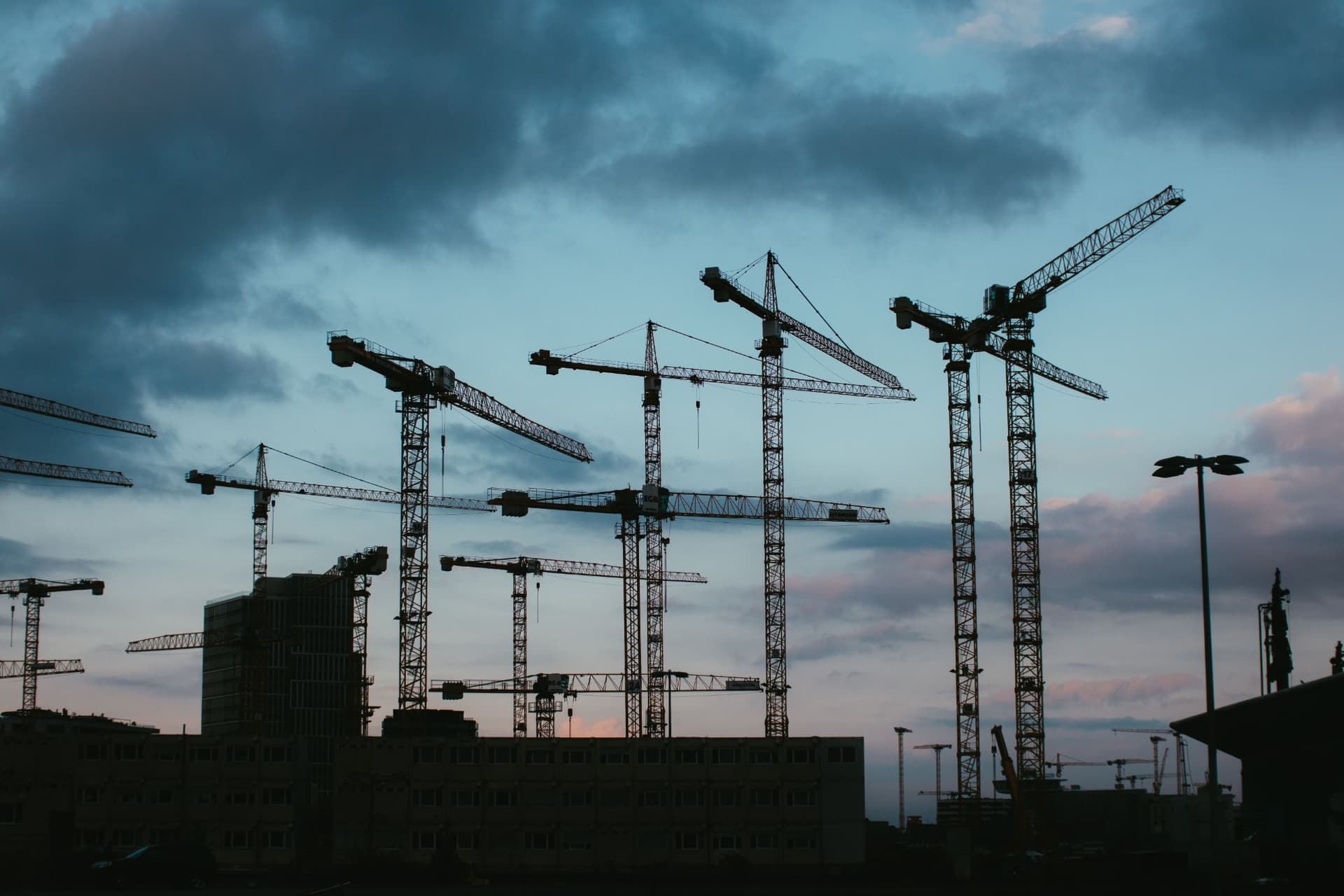 Silhouettes of tower cranes across a major construction skyline at dusk.
